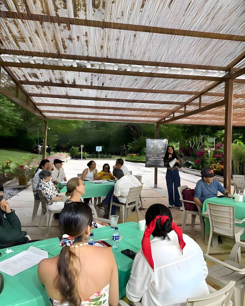 Un grupo en mesas de trabajo bajo la pérgola del taller, con el prado detrás.