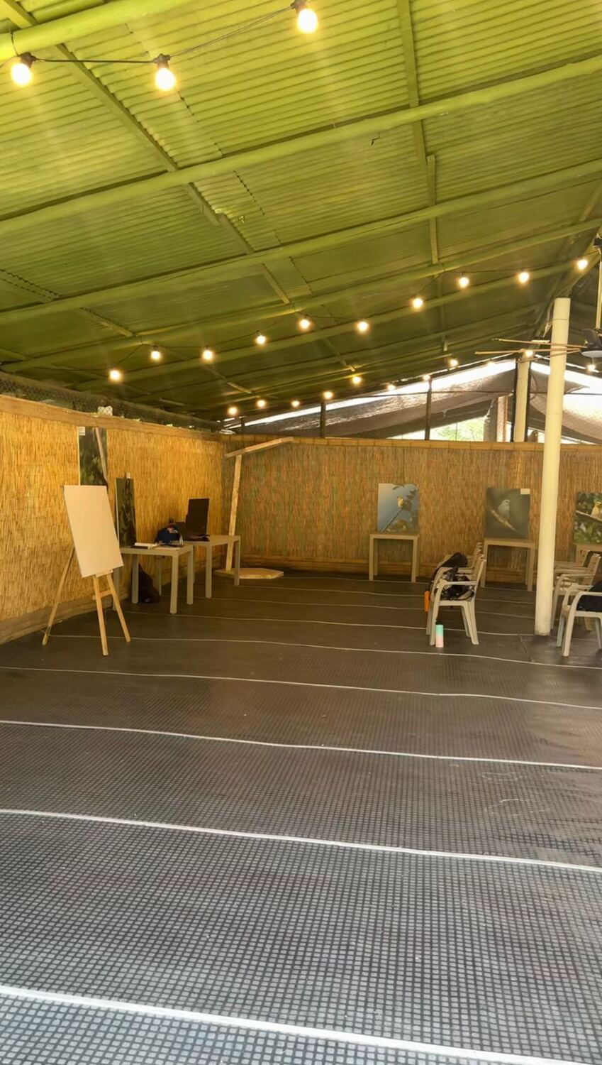 Covered Taller: a cane roof, woven-mat walls, string lights, an easel, and white Rimax chairs.