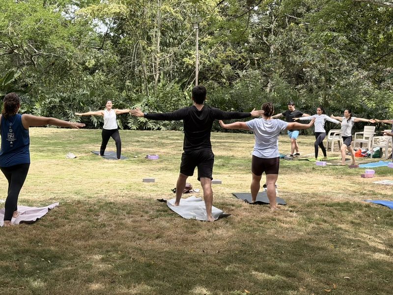 El grupo de la clase con los brazos abiertos sobre el pasto, rodeado de árboles.